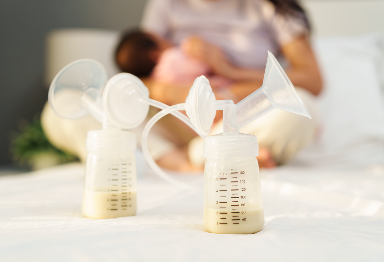 Newborn baby nursing with pumped milk in foreground.